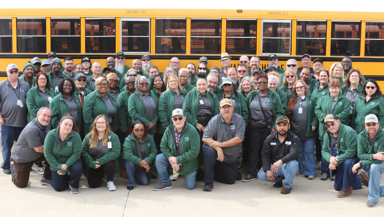 large group of adults in matching shirts in front of school bus